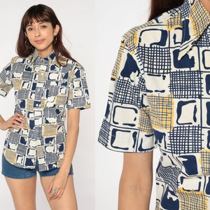 May include: A white short-sleeved button-down shirt with a geometric pattern in shades of blue and yellow. The shirt has a collar and a button-up front.