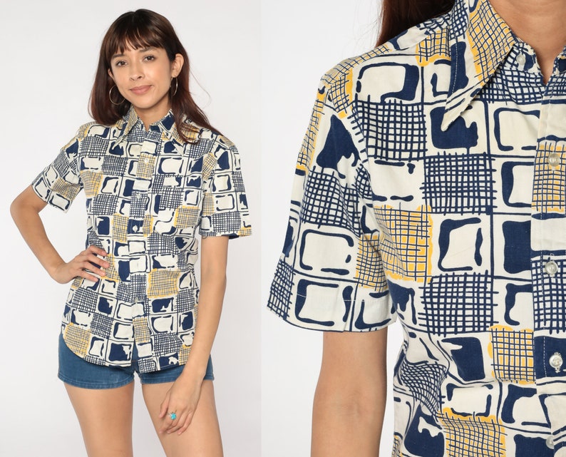 May include: A white short-sleeved button-down shirt with a geometric pattern in shades of blue and yellow. The shirt has a collar and a button-up front.