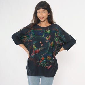 May include: Dark navy blue long-sleeve shirt with a colorful graphic print. The print features a scooter, fruit, and other abstract shapes. The shirt is made of a soft material and has a relaxed fit.