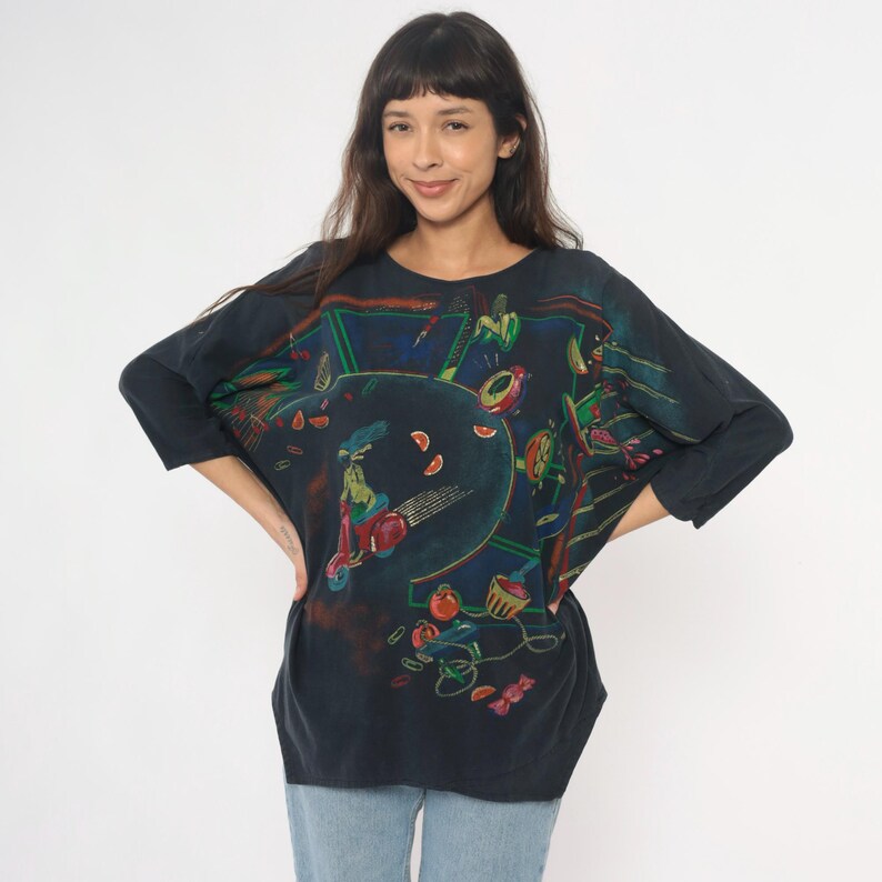 May include: Dark navy blue long-sleeve shirt with a colorful graphic print. The print features a scooter, fruit, and other abstract shapes. The shirt is made of a soft material and has a relaxed fit.
