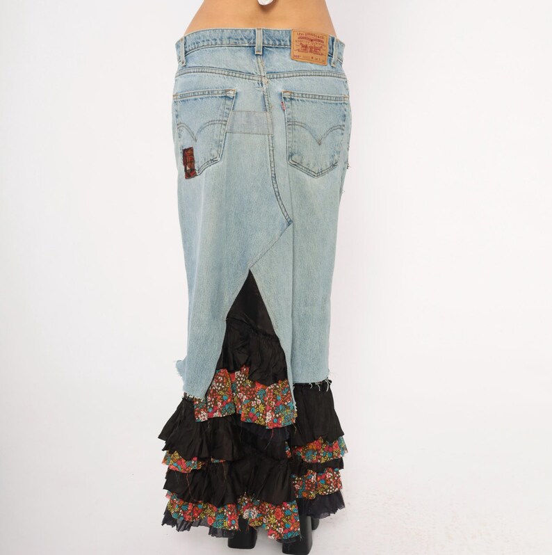 May include: Light blue denim skirt with a split back, featuring a black ruffled hem with a floral pattern. The skirt has a classic five-pocket design and a Levi's brand patch.