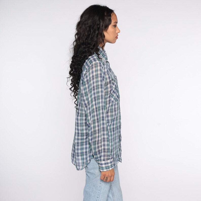 Op de afbeelding: Een geruit shirt met lange mouwen in tinten blauw, groen en wit. Het shirt heeft een knoopsluiting aan de voorkant, een borstzak en een klassieke kraag. Het shirt wordt gecombineerd met lichtblauwe jeans.