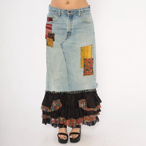 May include: A light blue denim skirt with colourful patchwork and a tiered black ruffle hem. The skirt has fabric patches in red, yellow, and floral patterns. The model is wearing black platform sandals.