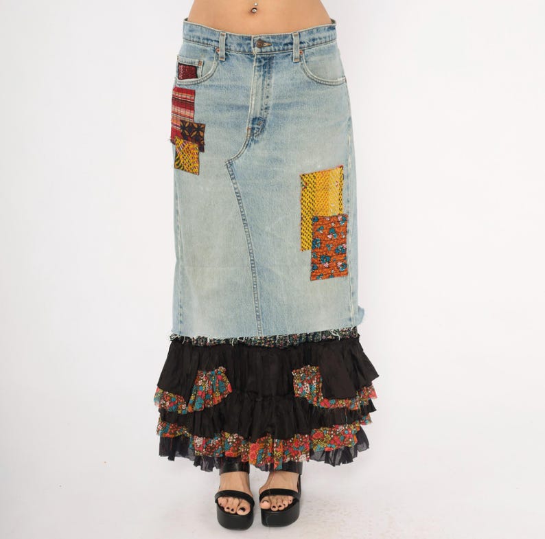 May include: A light blue denim skirt with colourful patchwork and a tiered black ruffle hem. The skirt has fabric patches in red, yellow, and floral patterns. The model is wearing black platform sandals.