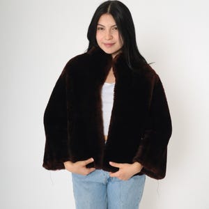 May include: A brown faux fur jacket with a collar and long sleeves. The jacket is open in the front and has a slightly cropped length.