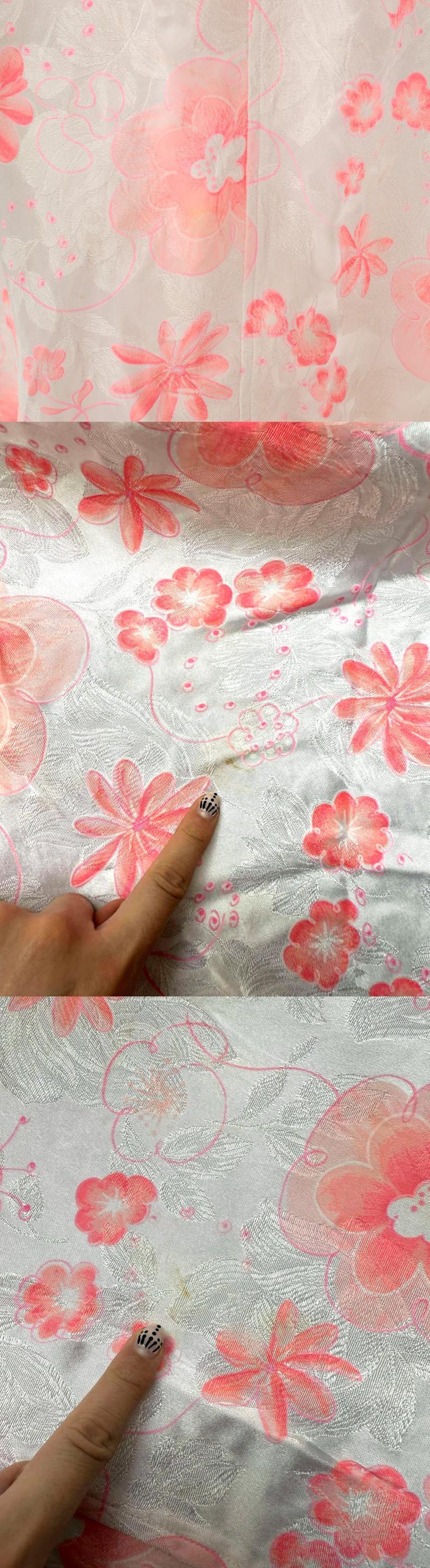 May include: A close-up of a fabric with a floral pattern. The fabric is white with a subtle texture, and features large, stylized flowers in shades of pink and coral. The design includes delicate stems and smaller floral accents.