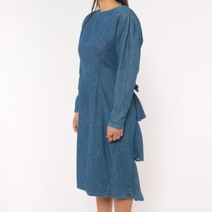Puede incluir: Un vestido de mezclilla de manga larga en un tono azul medio. El vestido presenta un cuello redondo, un corpi&ntilde;o ajustado con detalles de costuras verticales y una falda que llega hasta la rodilla. La tela tiene un tono azul uniforme.