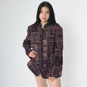 May include: A purple and black patterned button-up jacket with a mandarin collar. The jacket has a patchwork design with various geometric and floral patterns.