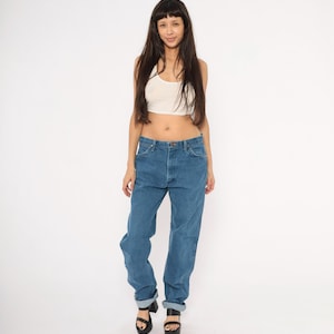 May include: A person wearing a white tank top and blue jeans. The jeans are cuffed at the ankles and have a classic, relaxed fit. The person is also wearing black platform sandals.