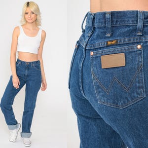 May include: A pair of high-waisted blue denim jeans with a classic straight leg fit. The jeans have a brown leather patch with the Wrangler logo on the back pocket.