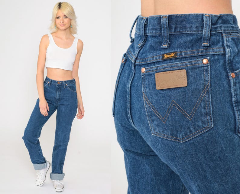 May include: A pair of high-waisted blue denim jeans with a classic straight leg fit. The jeans have a brown leather patch with the Wrangler logo on the back pocket.