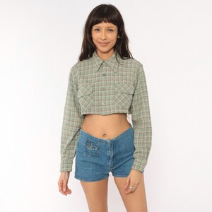 Puede incluir: Una camisa corta de manga larga con botones en un patr&oacute;n de cuadros verde salvia y rojo con dos bolsillos en el pecho, combinada con pantalones cortos de mezclilla azul con un bolsillo delantero peque&ntilde;o con bot&oacute;n y cierre de cremallera.