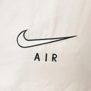 Puede incluir: Primer plano de una tela blanca con el logotipo de Nike swoosh bordado en negro y la palabra "AIR" debajo. El logotipo es una marca de verificaci&oacute;n curva y el texto est&aacute; en una fuente sans-serif.