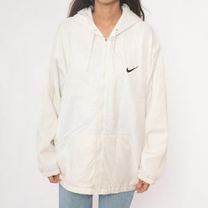 Puede incluir: Chaqueta con capucha Nike color crema con el logotipo negro de Nike en el pecho. La chaqueta tiene cierre de cremallera completa y capucha con cord&oacute;n. La chaqueta est&aacute; hecha de un material ligero.