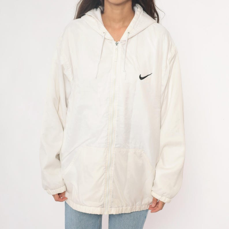 Puede incluir: Chaqueta con capucha Nike color crema con el logotipo negro de Nike en el pecho. La chaqueta tiene cierre de cremallera completa y capucha con cord&oacute;n. La chaqueta est&aacute; hecha de un material ligero.