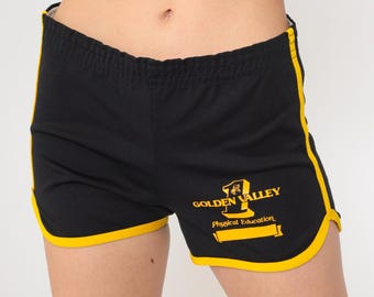 Può includere: Pantaloncini sportivi neri con bordino giallo e la scritta "Golden Valley Physical Education" stampata sul davanti.
