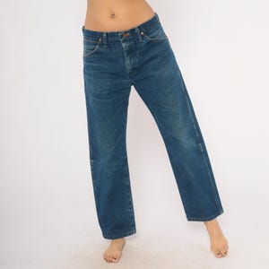 May include: Blue denim jeans with a classic straight leg fit. The jeans have a button and zipper closure, with front and back pockets. The denim has a slightly faded appearance, giving it a vintage look. The jeans are worn casually.