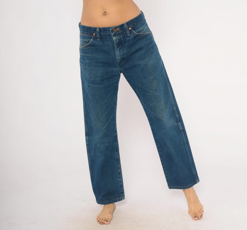 May include: Blue denim jeans with a classic straight leg fit. The jeans have a button and zipper closure, with front and back pockets. The denim has a slightly faded appearance, giving it a vintage look. The jeans are worn casually.