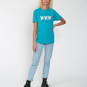 May include: A turquoise blue t-shirt with a graphic of three white cartoon bears wearing hats. The text "Love the Bears" is printed below the bears.