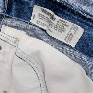 May include: Close-up of blue denim Wrangler jeans. The jeans have a white interior pocket and a label with the Wrangler logo and size information. The jeans are size 33 x 30.