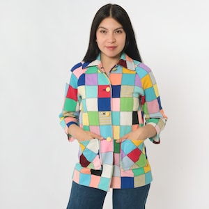 May include: A colorful patchwork jacket with a collar, two front pockets, and button closures. The jacket features a variety of square patches in shades of red, blue, green, yellow, and pink. The sleeves are long, and the jacket is worn by a person.