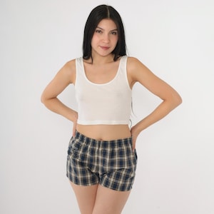 May include: A white tank top and blue and tan plaid shorts. The tank top is a scoop neck style. The shorts have an elastic waistband.