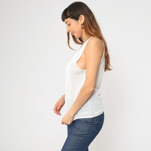 Peut inclure: Un d&eacute;bardeur blanc &agrave; col rond et &agrave; coupe ample. Le haut est associ&eacute; &agrave; un jean en denim bleu. Le mod&egrave;le se tient devant un fond blanc.
