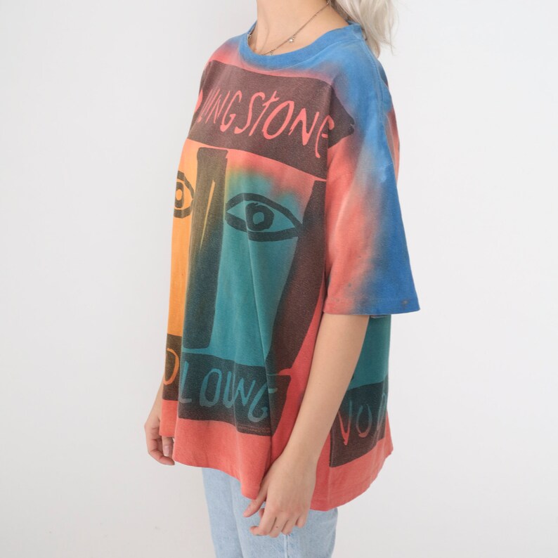 May include: A tie-dye t-shirt with a colorful abstract face design and the text "Rolling Stone" printed on the front.