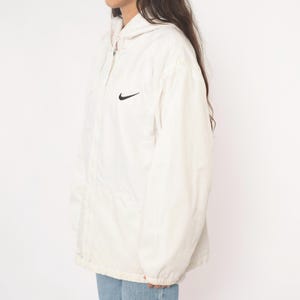 Puede incluir: Chaqueta con capucha Nike color crema con el logo negro de Nike en el pecho. La chaqueta tiene cremallera completa y capucha. Est&aacute; hecha de un material ligero y tiene un corte holgado. Chaqueta de estilo vintage.