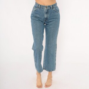 May include: Light blue denim jeans with a classic five-pocket design. The jeans have a straight leg fit and a button and zipper closure. The denim has a medium wash and a slight fade. The jeans are worn at the waist.