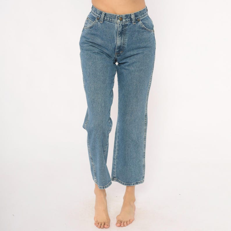 May include: Light blue denim jeans with a classic five-pocket design. The jeans have a straight leg fit and a button and zipper closure. The denim has a medium wash and a slight fade. The jeans are worn at the waist.