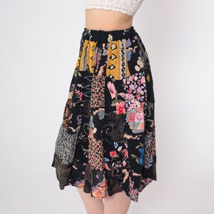 Op de afbeelding: Een zwarte midi-rok met een patchwork-ontwerp met bloemen-, geometrische en dierenprints in tinten roze, geel, blauw en bruin.