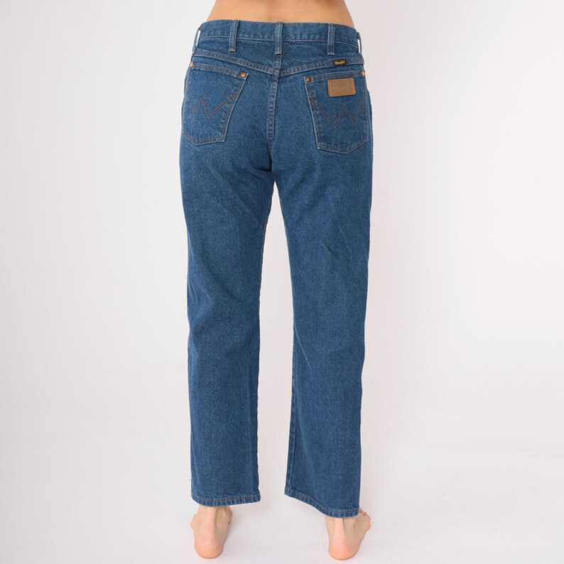 May include: A pair of blue denim jeans with a brown leather patch on the back pocket that says "Wrangler".