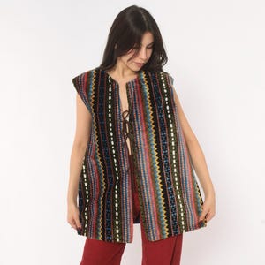 May include: A sleeveless vest featuring a vertical pattern of multicolored stripes, including shades of blue, pink, yellow, and green on a black background. The garment has a front opening secured with thin brown laces and a straight hemline.