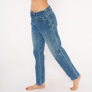 Pode incluir: Jeans azuis de ganga com um design cl&aacute;ssico de cinco bolsos. Os jeans t&ecirc;m um corte de perna reto e uma lavagem desbotada, dando-lhes um visual vintage. Os jeans s&atilde;o usados descal&ccedil;os.