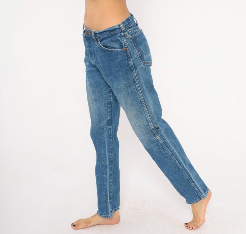 Pode incluir: Jeans azuis de ganga com um design cl&aacute;ssico de cinco bolsos. Os jeans t&ecirc;m um corte de perna reto e uma lavagem desbotada, dando-lhes um visual vintage. Os jeans s&atilde;o usados descal&ccedil;os.
