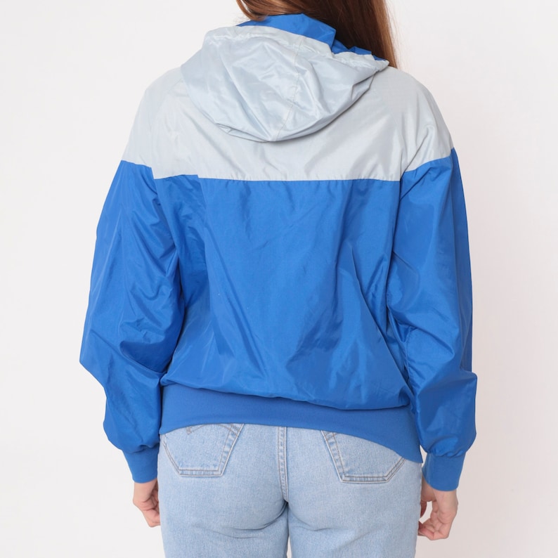 May include: A blue and light blue hooded jacket with a zipper closure. The jacket has a drawstring hood and a ribbed hem.