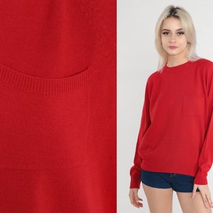 May include: A red long-sleeved sweater with a single patch pocket on the front.