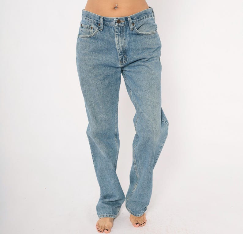Peut inclure: Jean bleu clair avec une coupe droite classique &agrave; cinq poches. Le jean a une fermeture &agrave; bouton et &agrave; glissi&egrave;re. Le denim a un d&eacute;lavage d&eacute;color&eacute;, lui donnant un aspect vintage. Le jean est port&eacute; par une personne.
