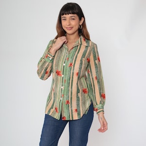 Peut inclure: Une chemise à rayures verticales beiges, vertes et noires, ornée de motifs floraux rouges. La chemise à manches longues est portée avec un jean bleu.