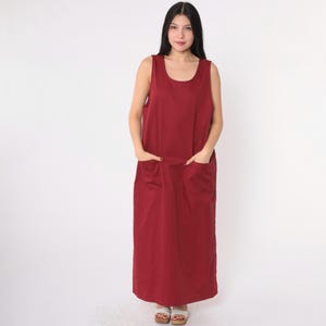 May include: A sleeveless maxi dress in a deep burgundy color. The dress has a scoop neck and two large pockets on the front.