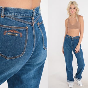 May include: High-waisted blue denim jeans with a cuffed hem. The jeans have a back pocket with embroidered detailing that reads "C.L.A.S.S.I.C."