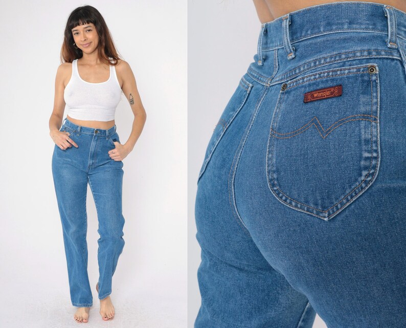 Op de afbeelding: Een paar blauwe denim jeans met een hoge taille en een klassieke rechte pijp. De jeans heeft een bruin leren patch met het woord "Wrangler" op de rechter achterzak.