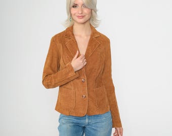 Puede incluir: Una blazer de pana marrón con cierre de dos botones y dos bolsillos delanteros. La blazer tiene una solapa con muescas clásica y se combina con vaqueros azules. La chaqueta es de un tono cálido y terroso.