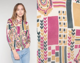 May include: A long-sleeved shirt with a geometric pattern in shades of pink, brown, and green. The pattern features a variety of shapes, including hearts, squares, and diamonds.