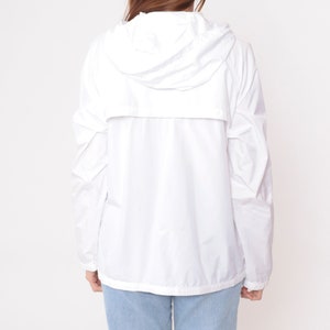 May include: A white hooded jacket with a full-length zipper and long sleeves. The jacket is made of a lightweight material and has a drawstring hood. The model is wearing blue jeans. The jacket is a casual outerwear piece.