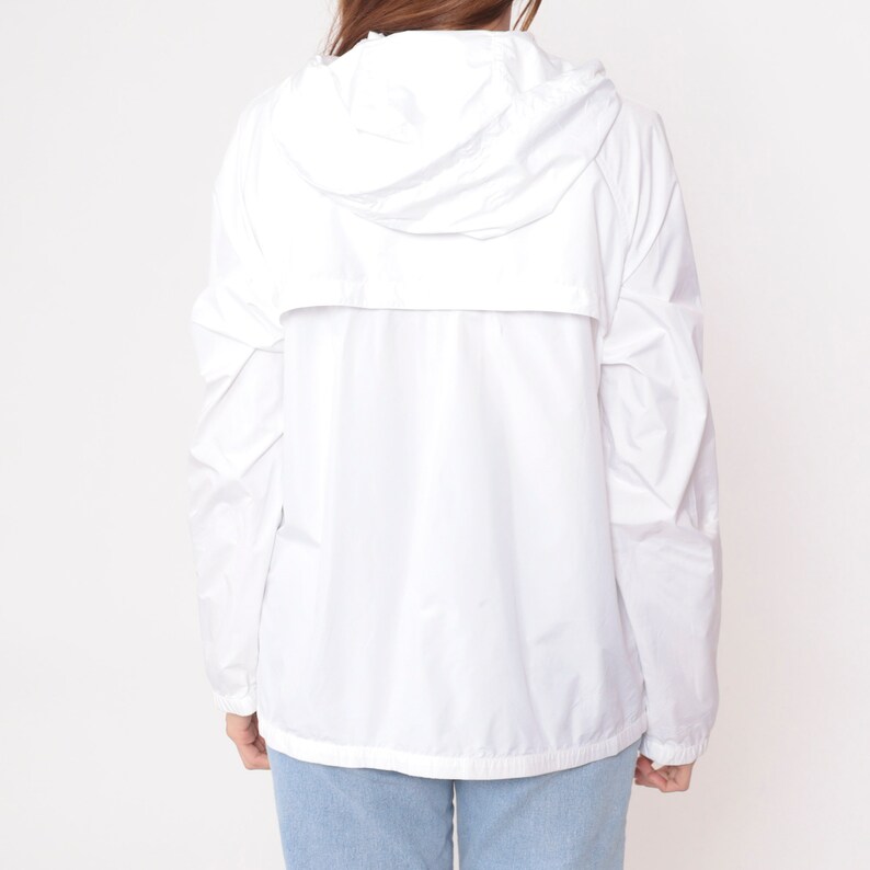 May include: A white hooded jacket with a full-length zipper and long sleeves. The jacket is made of a lightweight material and has a drawstring hood. The model is wearing blue jeans. The jacket is a casual outerwear piece.