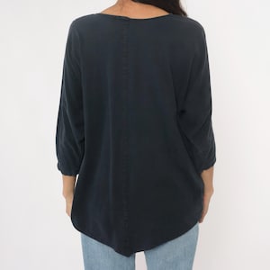 May include: A dark navy blue top with three-quarter sleeves. The top has a scoop neckline and a relaxed fit. The back of the top features a vertical seam down the center. The model is wearing blue jeans.