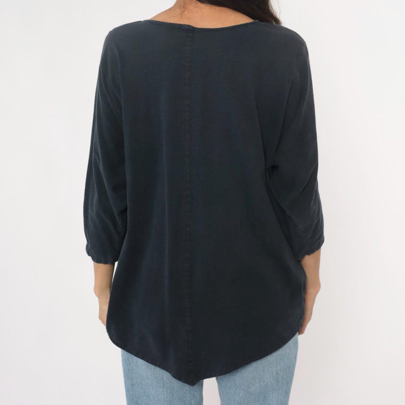 May include: A dark navy blue top with three-quarter sleeves. The top has a scoop neckline and a relaxed fit. The back of the top features a vertical seam down the center. The model is wearing blue jeans.