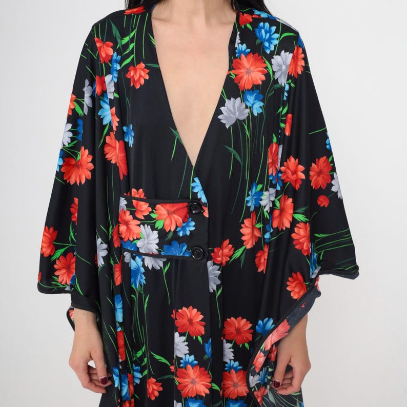 May include: A black long-sleeved dress with a deep V-neckline and a floral print featuring red, blue, and white flowers. The dress has a button closure at the front and a fitted silhouette.